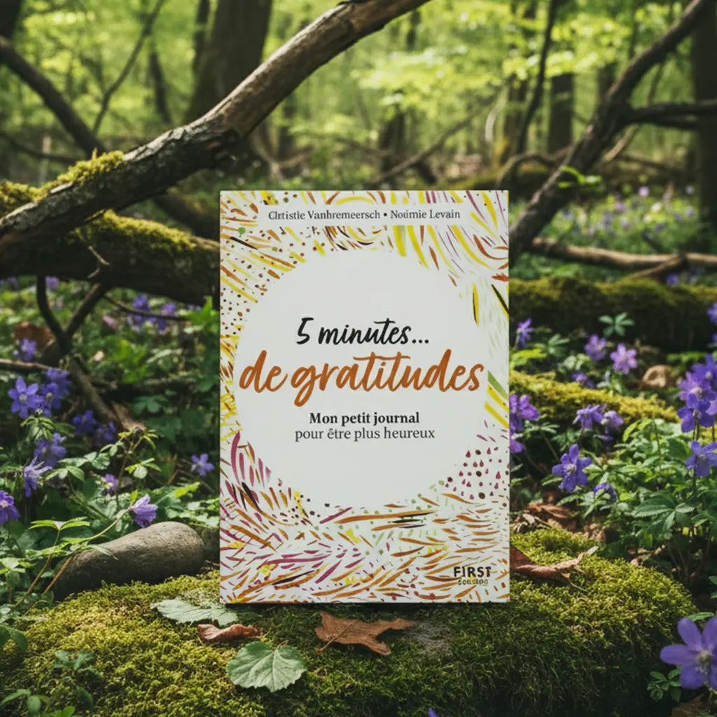 Livre coloré 5 Minutes de Gratitude de Christie Vanbremeersch posé sur une souche en forêt, couverture blanche tachetée de motifs joyeux jaunes et rouges.