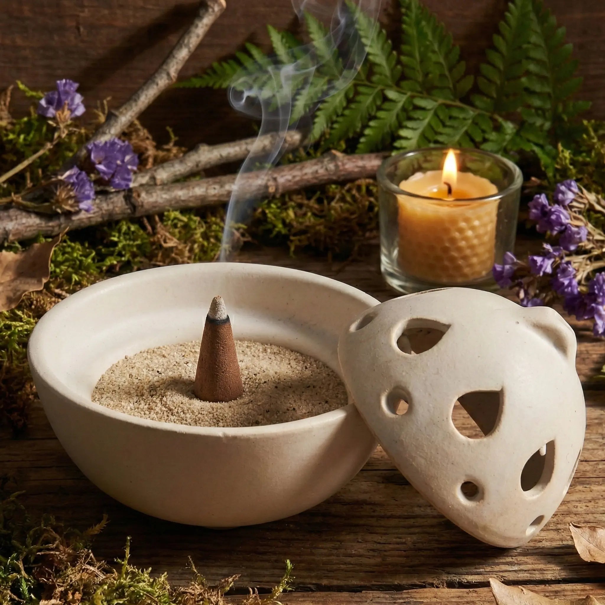 Brûle-encens en céramique blanche, forme goutte ajourée, pour cônes d’encens, présenté ouvert sur décor naturel.
