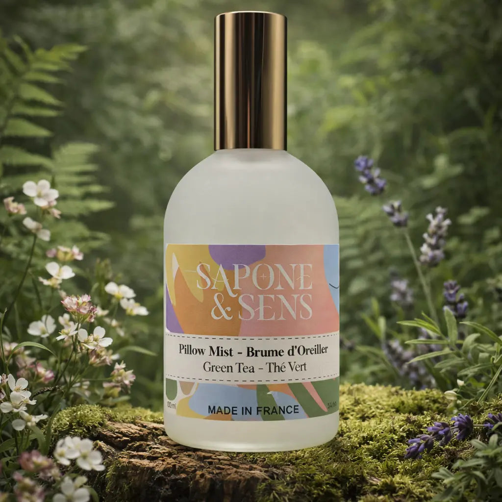 Flacon givré de brume d'oreiller posé sur une souche moussue, entouré de fleurs blanches et de brins de lavande dans une forêt baignée de lumière.