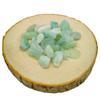 Un tas de petites pierres d'aigue-marine roulées aux nuances vert d'eau et bleu pâle translucides, disposé sur une rondelle de bois clair.