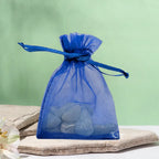 Un petit sac en organza bleu contenant des pierres d'aigue-marine roulées (taille XS), posé sur une pierre plate naturelle devant un arrière-plan vert clair.