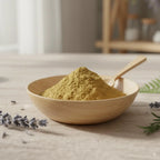 Encens d'Aloès en poudre de couleur vert olive, formant un monticule dans un bol en bois clair avec une cuillère, entouré de brins de lavande et de romarin.