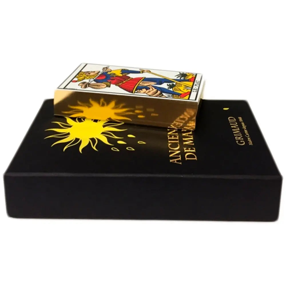 Coffret luxe « Ancien Tarot de Marseille » (Grimaud) : grande boîte noire rigide posée à plat, décorée d’un soleil jaune stylisé et du titre doré ; un paquet de cartes est posé sur le couvercle, laissant apparaître une carte du tarot sur le dessus (L’Échoppe de Gaïa).