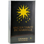 Coffret « Ancien Tarot de Marseille » (Grimaud) : boîte noire (filmée) avec un grand soleil jaune stylisé en haut et petits motifs jaunes dessous ; titre « ANCIEN TAROT DE MARSEILLE » en lettres dorées au centre ; mention « GRIMAUD – Maître Cartier depuis 1848 » en bas (L’Échoppe de Gaïa).