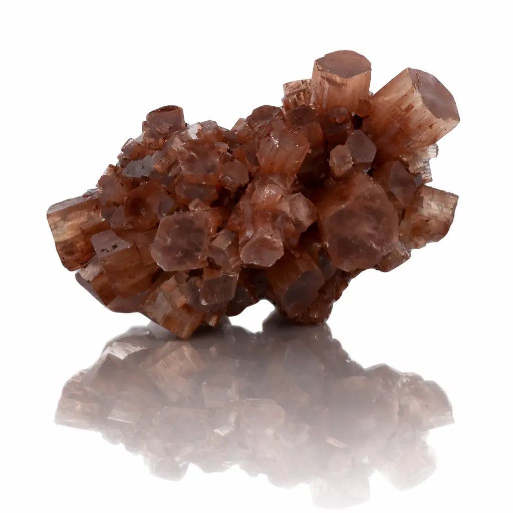 Un cristal d'aragonite brut présentant un agrégat de prismes hexagonaux aux teintes brunes et orangées, posé sur un fond blanc avec un reflet net.