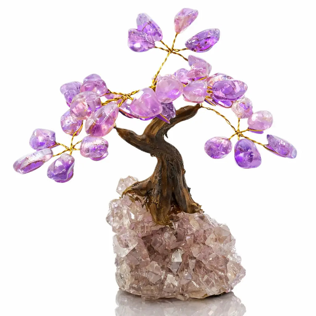 Une vue d'ensemble d'un petit arbre du bonheur montrant son tronc sculpté et ses feuilles en améthyste violette, solidement fixé sur une base de cristal de roche brut sur fond blanc.