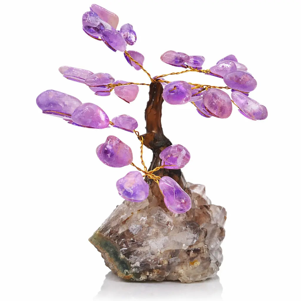Un petit arbre du bonheur décoratif aux feuilles en améthyste, doté d'un tronc brun et de branches en fil doré, fixé sur une base de cristal de roche brut sur fond blanc.