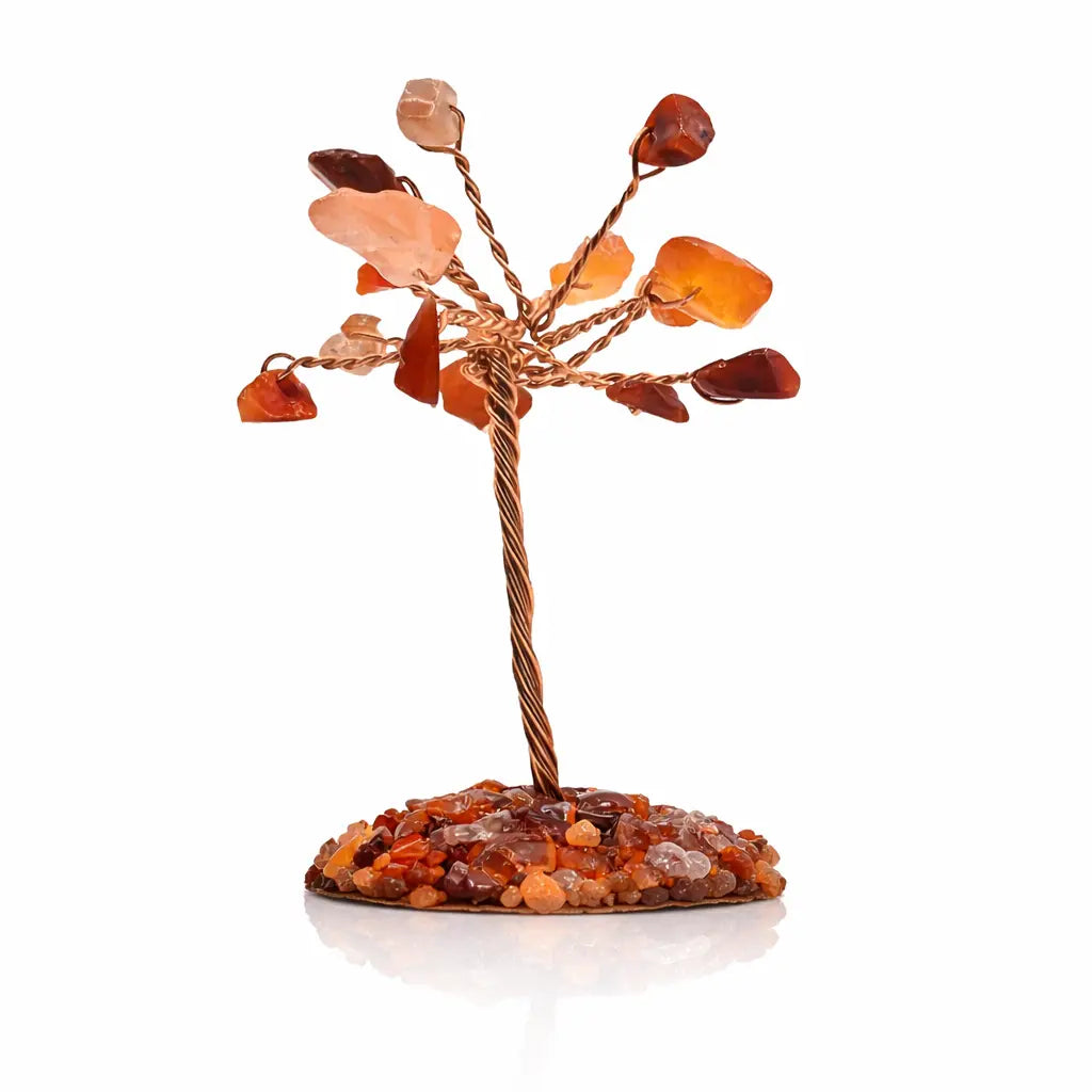 Un arbre du bonheur miniature composé d'un tronc en fils de cuivre torsadés et de feuilles en cornaline aux nuances orangées, reposant sur un socle couvert de petits éclats de pierres assorties sur un fond blanc avec reflet.