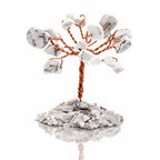 Un arbre du bonheur décoratif miniature composé d'un tronc en fil de cuivre torsadé et de feuilles en pierres de howlite blanche, fixé sur un socle de petits éclats minéraux assortis, présenté sur fond blanc.