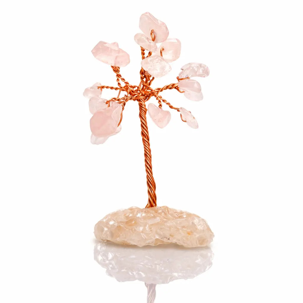 Un arbre du bonheur décoratif miniature avec un tronc en fil de cuivre torsadé et des feuilles en pierres de quartz rose, monté sur un socle d'éclats minéraux clairs, présenté sur un fond blanc.