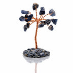 Un arbre du bonheur décoratif composé d'un tronc en fil de cuivre torsadé et de feuilles en pierres de sodalite bleue, fixé sur un socle de petits éclats minéraux assortis, présenté sur fond blanc.