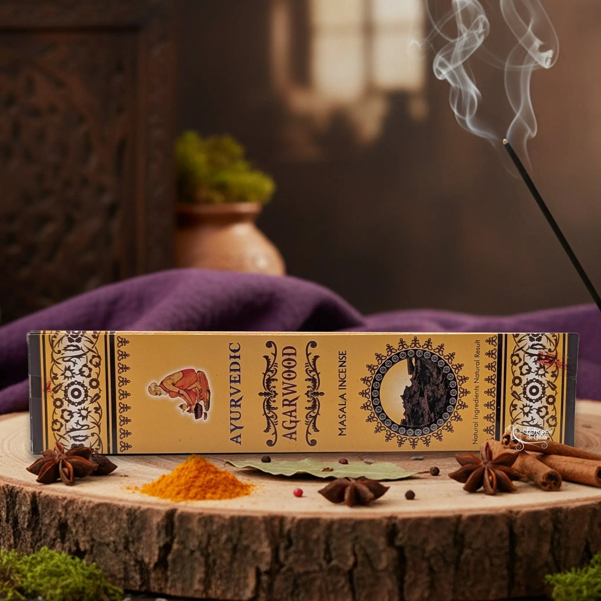 Boîte d'encens "Ayurvedic Agarwood Masala" sur une rondelle de bois, avec épices et encens fumant.