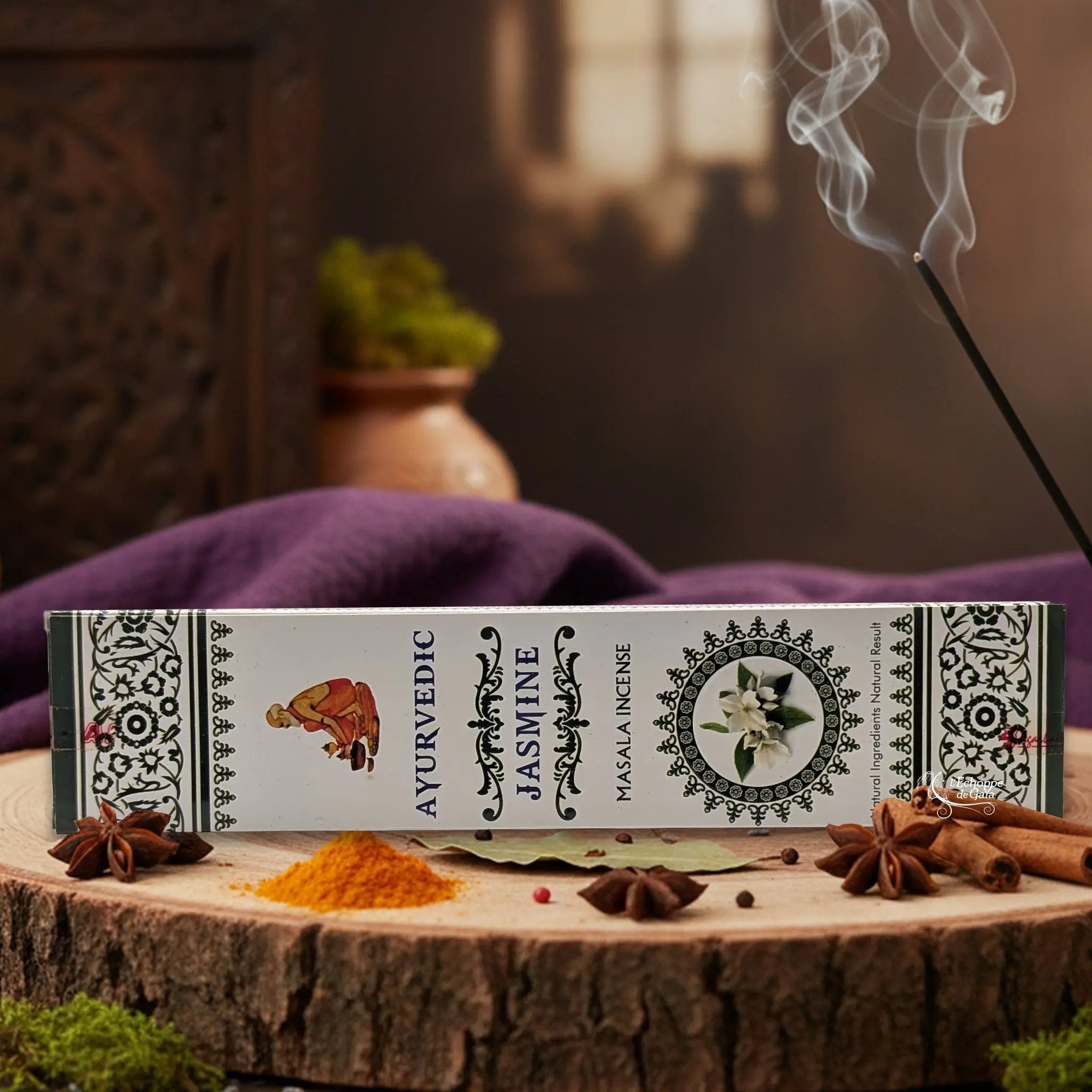 Boîte d'encens "Ayurvedic Jasmine Masala" sur une rondelle de bois, avec épices et encens fumant.