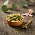 Grains d'encens de résine Bergamote, mélange de teintes jaune-vert citron et vert foncé, dans un bol en bois avec cuillère, sur une planche de bois rustique.