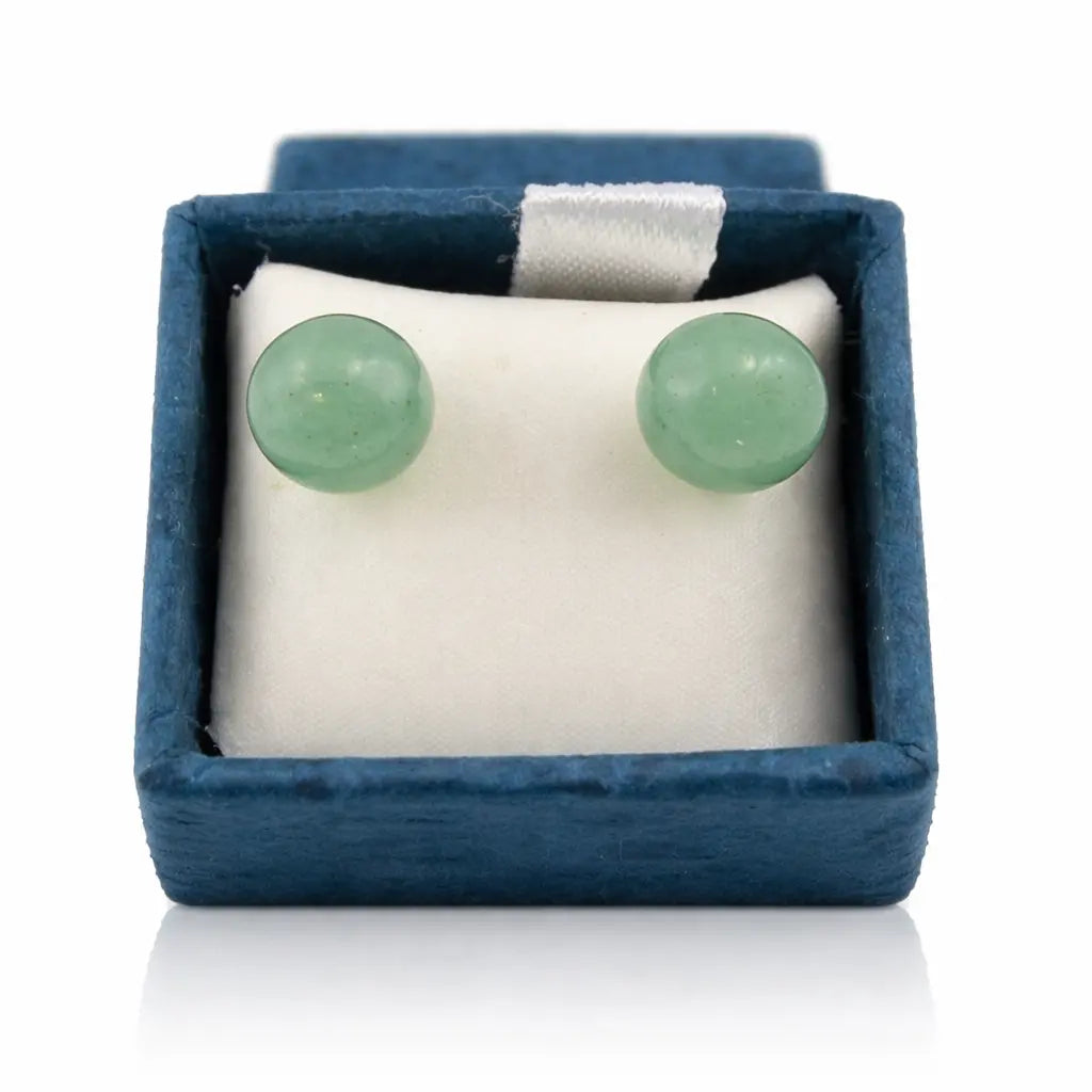 Une paire de boucles d'oreilles puces en aventurine verte, présentant deux perles rondes aux nuances naturelles, soigneusement disposées dans leur écrin bleu sur un coussinet blanc.