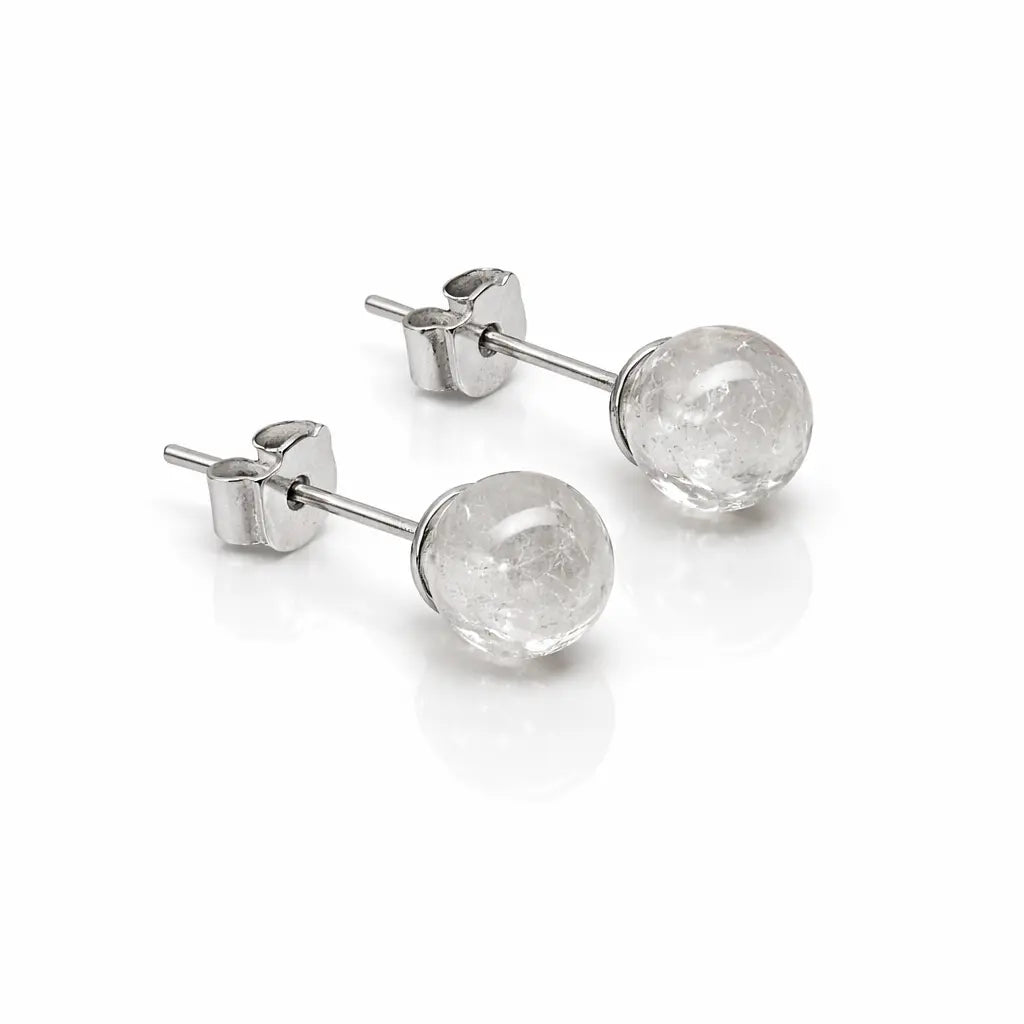 Une paire de boucles d'oreilles puces en argent, ornées de perles rondes en cristal de roche transparent aux inclusions naturelles givrées, présentées sur un fond blanc avec reflet.