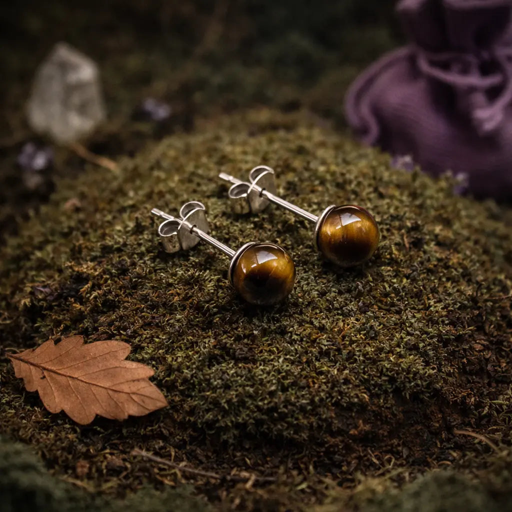 Paire de boucles d'oreilles clous aux perles d'oeil de tigre chatoyantes, alternant entre l'or et le brun, posées sur un lit de mousse forestière sauvage.