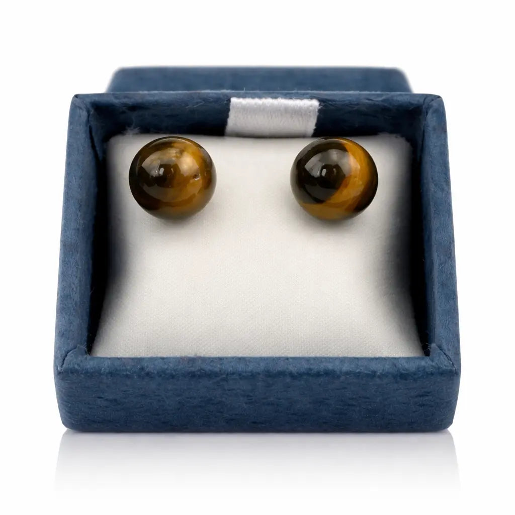 Une paire de boucles d'oreilles puces en œil de tigre, présentant deux perles rondes aux reflets dorés et marron, soigneusement disposées dans leur écrin bleu sur un coussinet blanc.