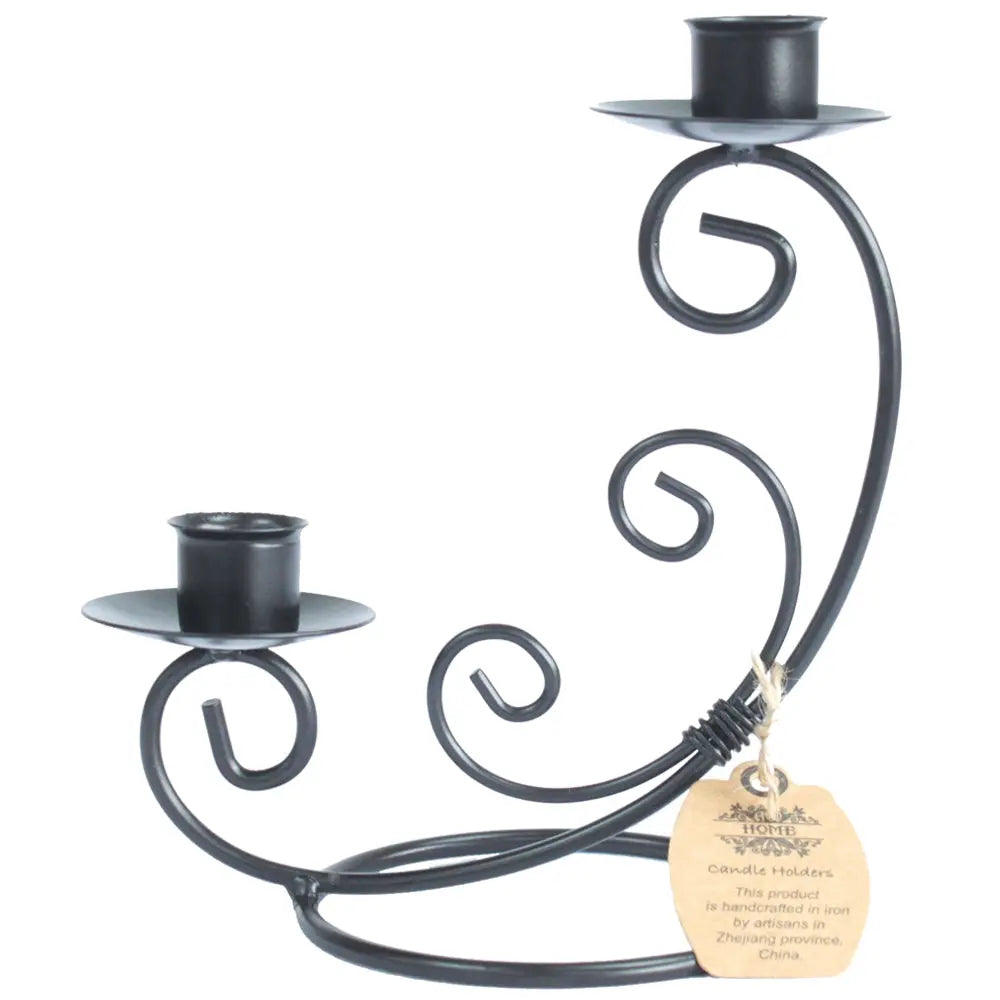 Un bougeoir double en fer forgé noir, caractérisé par ses volutes décoratives et ses deux coupelles réceptacles à des hauteurs différentes, présenté sur un fond blanc avec une étiquette artisanale.