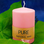 Bougie pilier rose en cire naturelle « PURE », avec étiquette beige, posée sur des feuilles vertes (L’Echoppe de Gaïa).