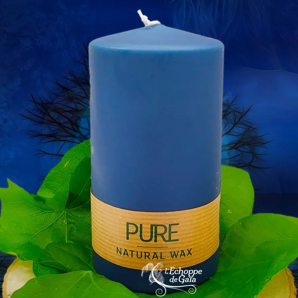 Bougie pilier bleu nuit en cire naturelle « PURE », avec étiquette beige, posée sur des feuilles vertes (L’Echoppe de Gaïa).