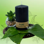 Bougie pilier noire en cire naturelle « PURE », avec étiquette kraft, posée sur une feuille verte avec plante succulente (L’Echoppe de Gaïa).