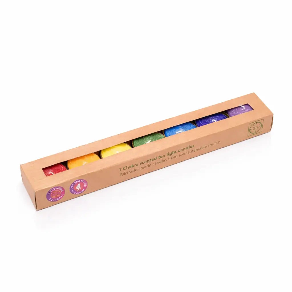Un coffret de sept bougies chauffe-plat aux couleurs des 7 chakras, présentées dans un étui en carton kraft avec fenêtre transparente, sur un fond blanc.