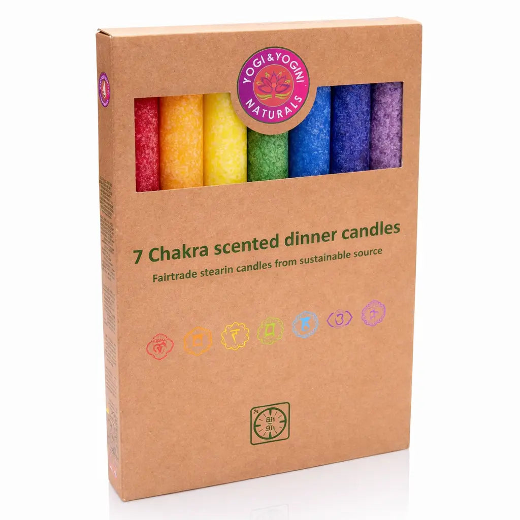 Un coffret de sept bougies flambeaux aux couleurs des 7 chakras de la marque Yogi & Yogini Naturals, présentées dans un étui en carton kraft avec fenêtre, posé sur un fond blanc.
