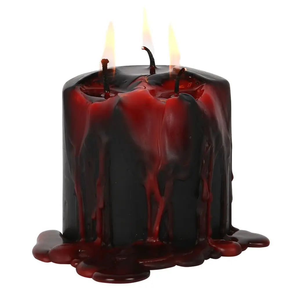 Une bougie pilier noire basse à trois mèches allumée, dont la cire rouge sang coule abondamment sur les parois et s'accumule à sa base, présentée sur un fond blanc.