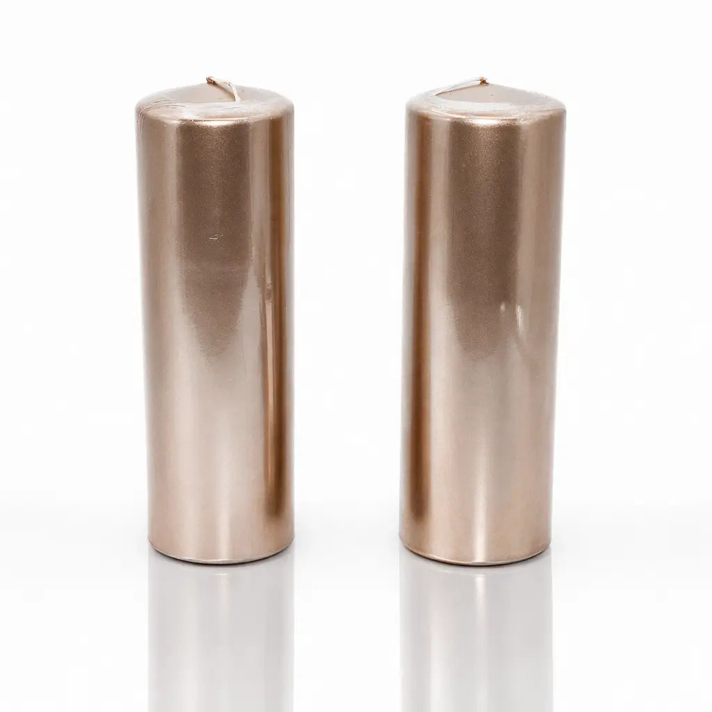 Un lot de deux bougies piliers métallisées de couleur or rose (ou vieux rose), de forme cylindrique, présentées debout sur un fond blanc avec un reflet à leur base.