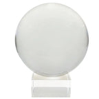 Boule de cristal transparente sur fond blanc, avec une sphère parfaitement centrée et un léger reflet sur le bord droit. Elle est posée sur un socle cubique en verre/plexi transparent, aux arêtes bien nettes.