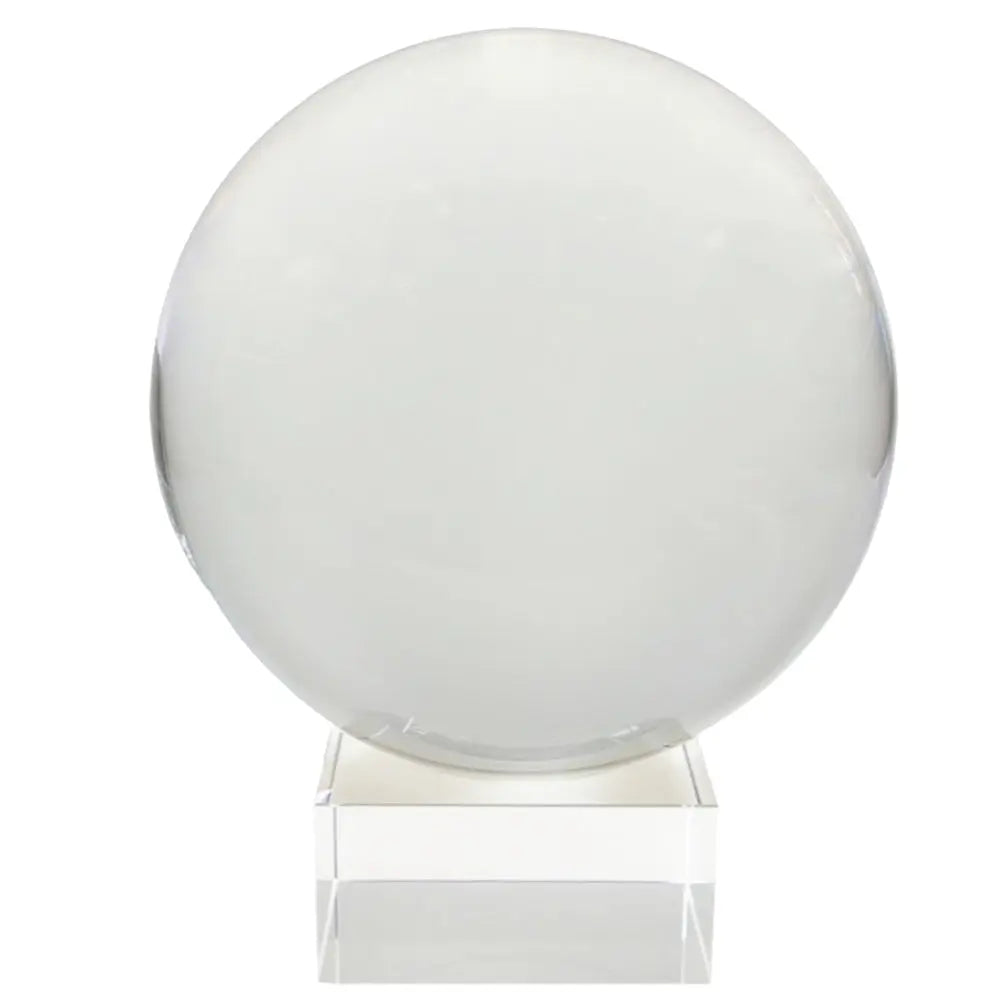 Boule de cristal transparente sur fond blanc, avec une sphère parfaitement centrée et un léger reflet sur le bord droit. Elle est posée sur un socle cubique en verre/plexi transparent, aux arêtes bien nettes.