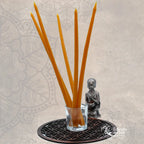Cinq cierges fins en cire d'abeille jaune dans un verre, posés sur une Fleur de Vie avec une statuette de Bouddha.