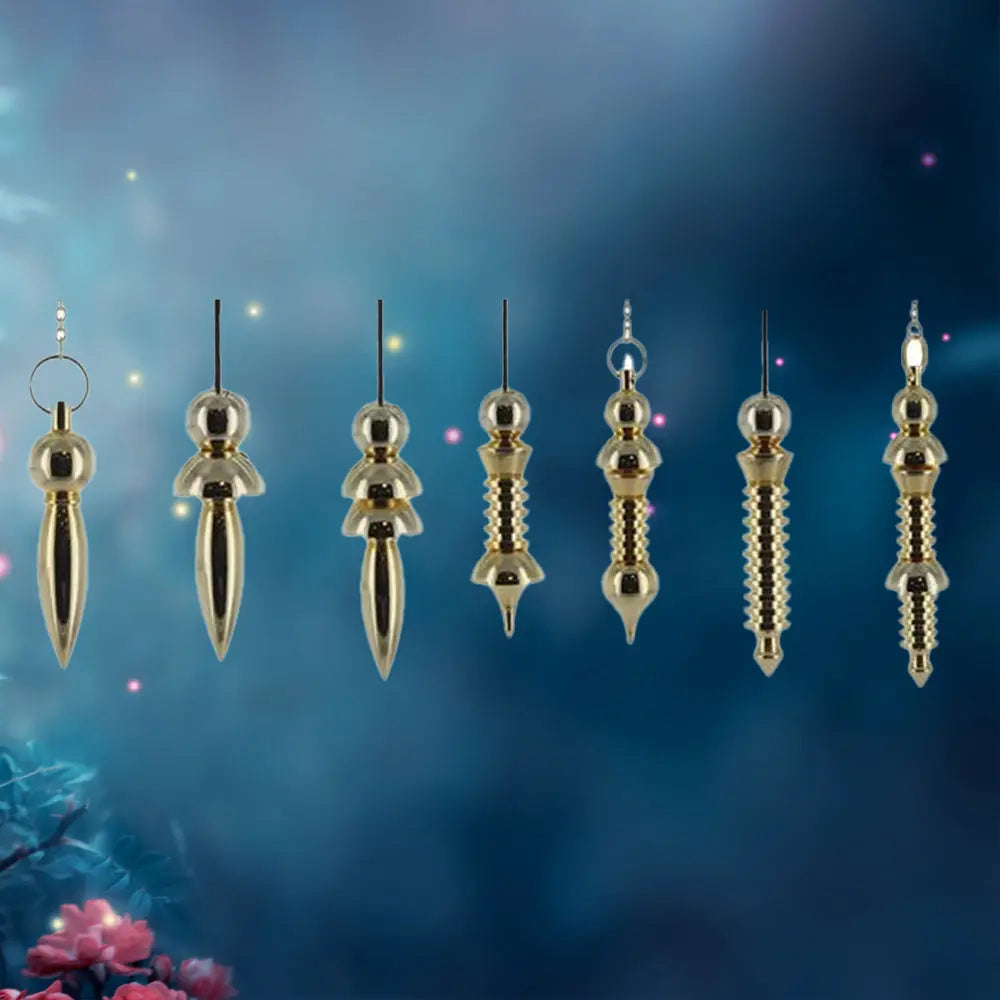 Alignement de sept pendules égyptiens en métal doré (type Thot ou Isis), présentant des variations dans le nombre de disques et la forme de la pointe pour moduler leur sensibilité vibratoire.