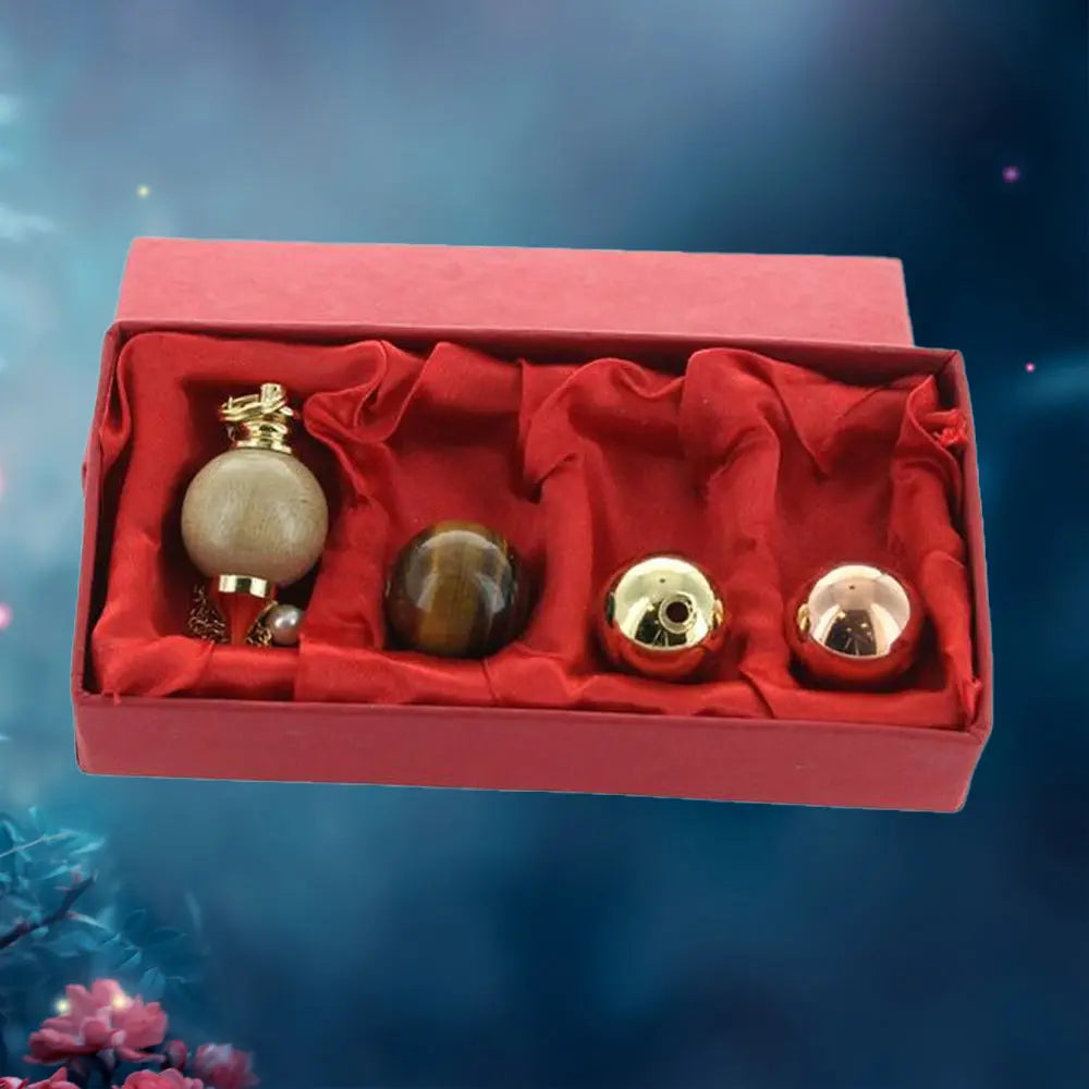 Coffret rouge contenant un ensemble de pendules de type Séphoroton, incluant un modèle monté avec une sphère en bois clair, ainsi que trois sphères interchangeables : une en œil-de-tigre et deux en métal (doré et cuivré).