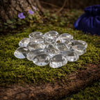 Ensemble de pierres de cristal de roche polies d'une transparence cristalline et lumineuse, disposées sur un tronc moussue avec un pochon bleu en arrière-plan.