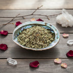 Coupelle en nacre remplie de feuilles de damiana séchées vert pâle sur table en bois décorée de cristaux et pétales de rose.