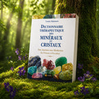 Livre Dictionnaire Thérapeutique des Minéraux et Cristaux de Louis Adamant posé contre un tronc d'arbre moussu, illustré de cristaux violets et de motifs ésotériques dorés.
