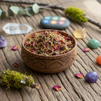 Bol en bois gravé rempli de mélange d’encens pour le chakra sacré, avec herbes et pétales colorés, posé sur une table en bois entourée de cristaux.