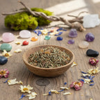 Bol en bois rempli de mélange d’encens aux herbes et résine, posé sur une table en bois avec fleurs séchées, cristaux et mousse décorative autour.