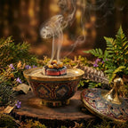 Encensoir en laiton doré, bol décoré motifs rouges et bleus, sable avec charbon et résine fumante, couvercle à côté, décor forêt.