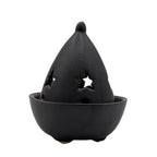 Brûle-encens en céramique noire mate, bol rond avec petits pieds, couvercle en forme de goutte ajouré d’étoiles, présenté fermé sur fond blanc.