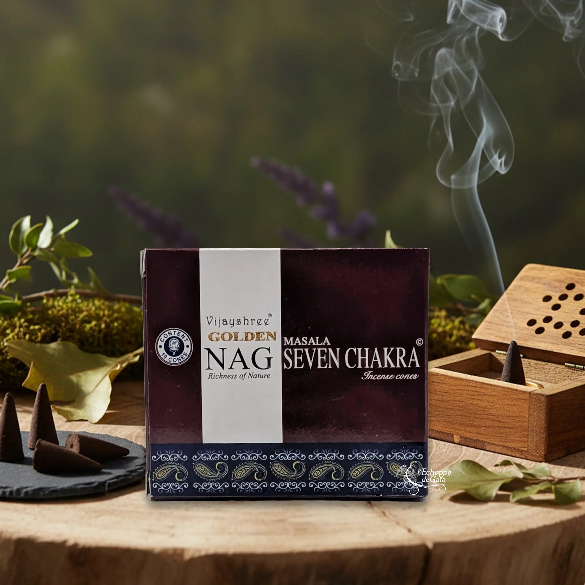 Boîte d'Encens Golden Nag Seven Chakra posée sur une tranche de bois, à côté de cônes d'encens bruts et d'une boîte porte-encens en bois diffusant de la fumée.