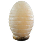 Lampe en véritable Sel de l'Himalaya - Forme Œuf Strié, illustrée éteinte, mettant en valeur la teinte naturelle rose pâle et l'aspect cristallin du bloc de sel sculpté de rainures horizontales sur son petit socle en bois clair.