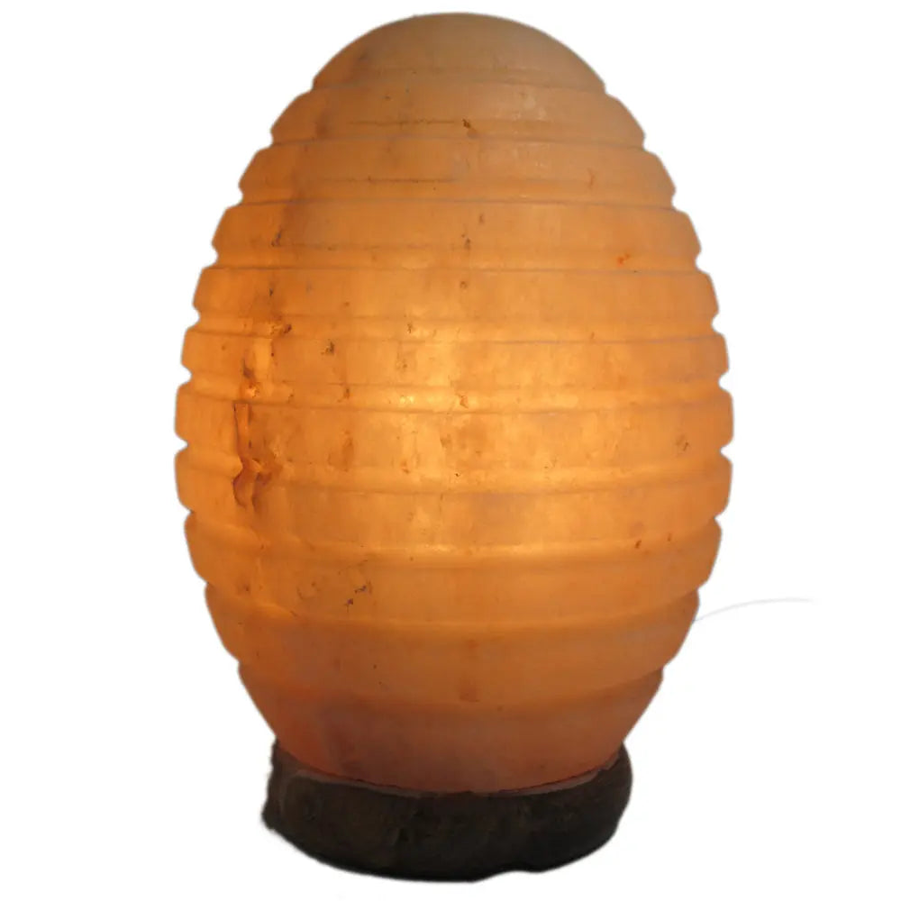 Lampe en véritable Sel de l'Himalaya - Forme Œuf Strié, illustrée par un bloc de sel taillé en forme d'œuf aux rainures horizontales régulières, diffusant une lueur douce, orangée et tamisée depuis son socle en bois.