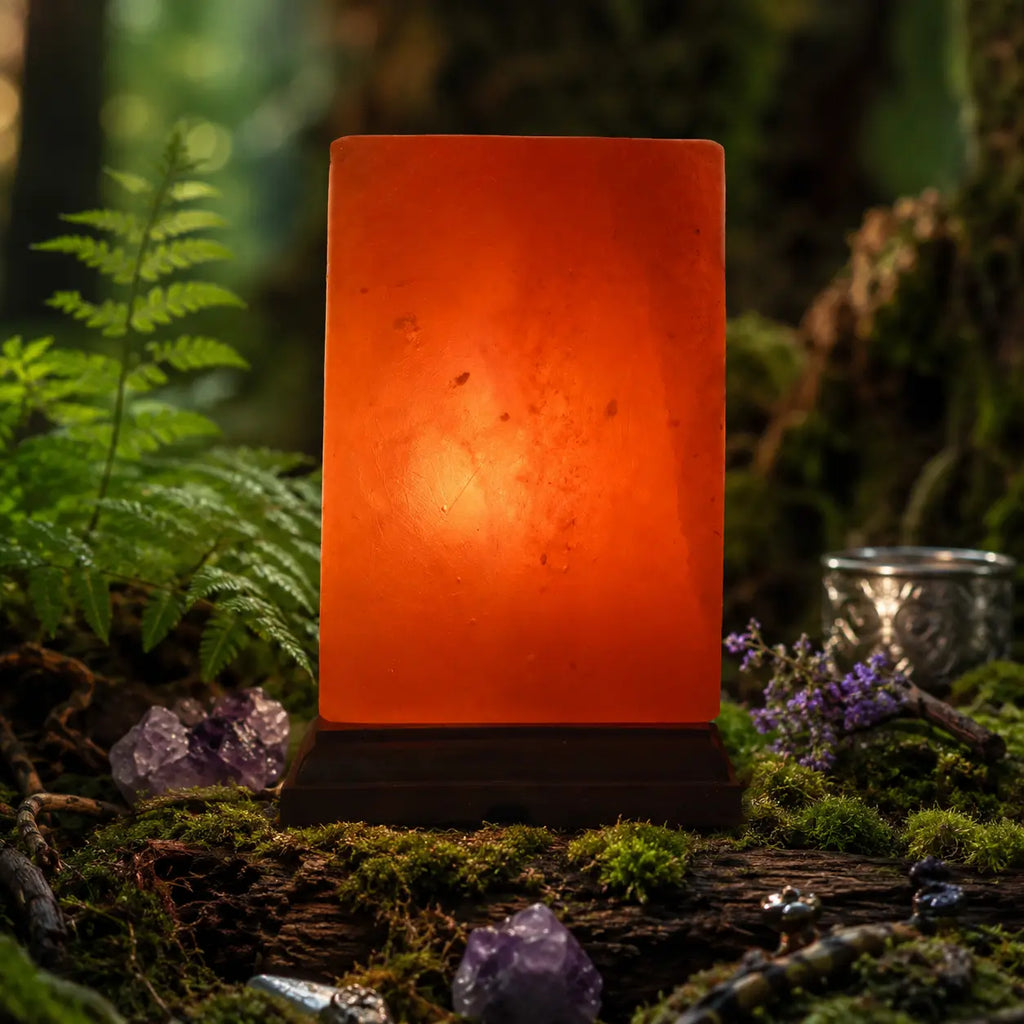 Lampe cube en sel de l'Himalaya allumée diffusant une lumière orange chaleureuse, posée sur un tronc moussue en forêt mystique entourée de cristaux d'améthyste.