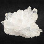 Amas de cristal de roche brut à pointes multiples translucides sur un fond noir.
