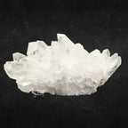 Amas de cristal de roche brut à pointes multiples translucides sur un fond noir texturé.