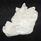 Gros plan d'un cristal de roche quartz translucide avec des pointes cristallines facettées sur un fond noir profond.