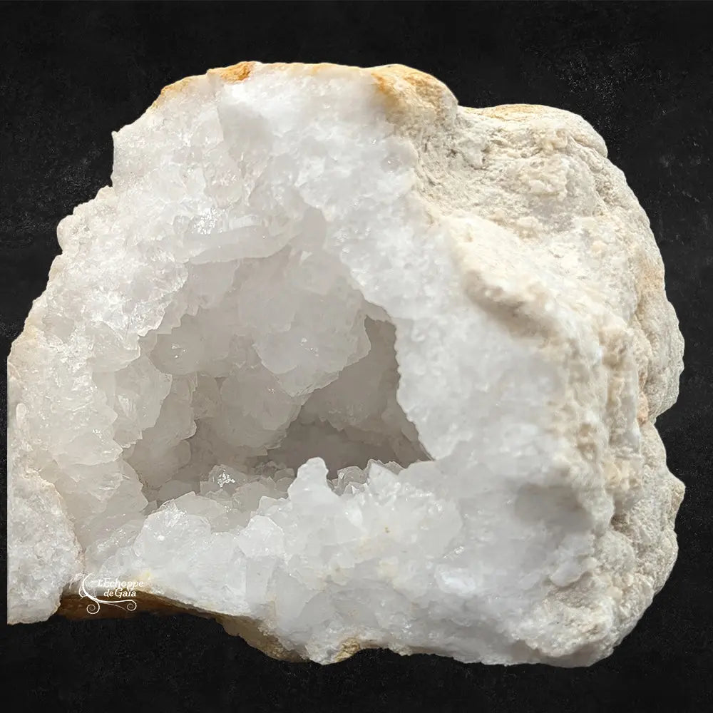 Zoom sur l'intérieur d'une géode de quartz blanc montrant des amas de cristaux translucides et une croûte mate.